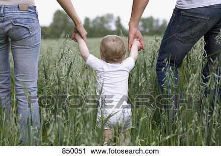 Two parents teaching their baby daughter to walk View Large Photo Image Stock Image - Two parents teaching their baby daughter to walk. Fotosearch