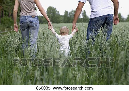 Stock Photography - Two parents walking in a field with their daughter. Fotosearch