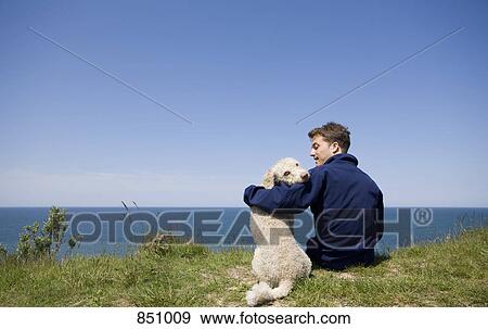 A man with his arm around a dog sitting by the sea View Large Photo Image Stock Photo - A man with his arm around a dog sitting by the sea. Fotosearch