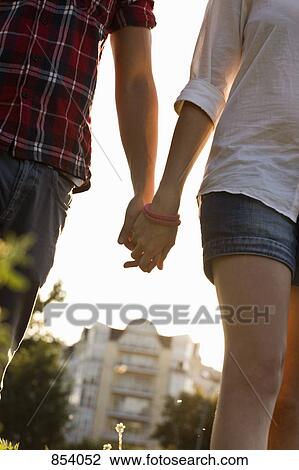 Stock Image - A young couple holding hands in a park. Fotosearch