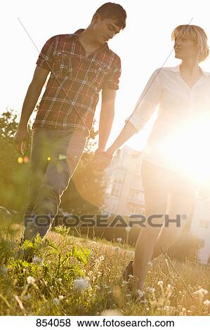 Stock Photo - A young couple holding hands walking through a park, front view. Fotosearch