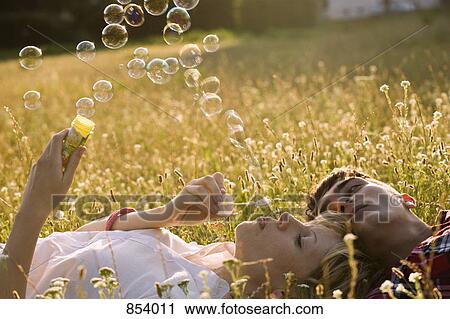 Stock Image - A young couple in a field blowing bubbles. Fotosearch