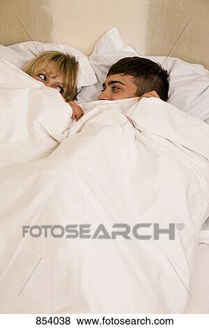 A young couple in bed with the duvet pulled up to their eyes View Large Photo Image Stock Photo - A young couple in bed with the duvet pulled up to their eyes. Fotosearch