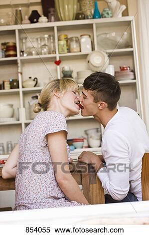 Stock Photography - A young couple kissing with a strawberry. Fotosearch