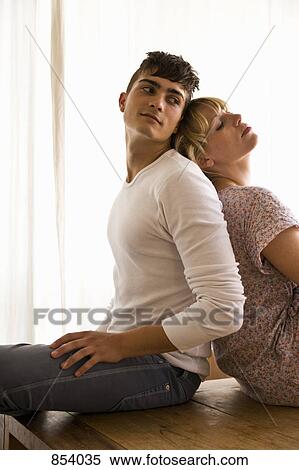 Stock Photography - A young couple sitting back to back on a table. Fotosearch