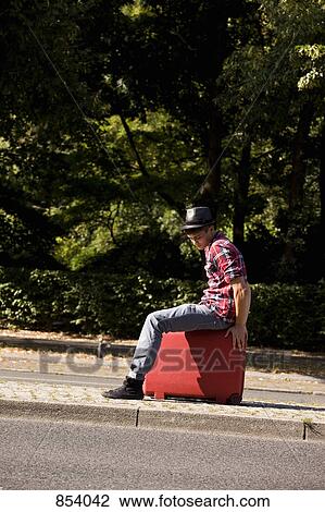A young man sitting on a suitcase View Large Photo Image Stock Image - A young man sitting on a suitcase. Fotosearch