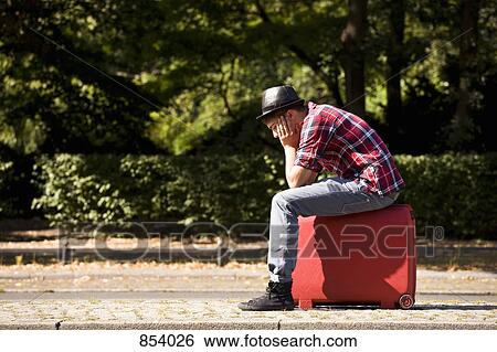 Stock Photograph - A young man sitting on a suitcase. Fotosearch