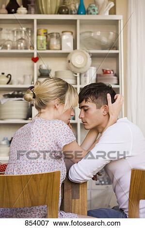 Stock Photo - A young passionate couple sitting in a domestic kitchen. Fotosearch