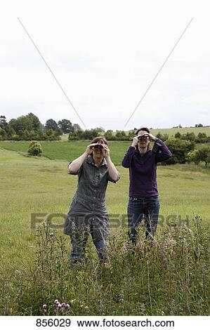 Stock Photo - Two women standing in a field and using binoculars. Fotosearch