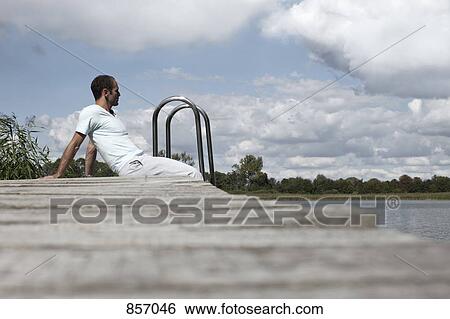 A man sitting on a spa jetty staring off into the distance View Large Photo Image Stock Photograph - A man sitting on a spa jetty staring off into the distance. Fotosearch