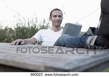 A man sitting at an outdoor table reading a magazine, non-urban scene View Large Photo Image Stock Image - A man sitting at an outdoor table reading a magazine, non-urban scene. Fotosearch