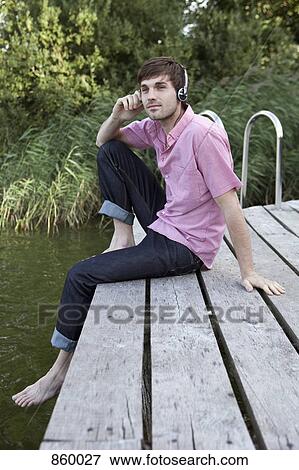 Stock Photo - A man wearing headphones relaxing on a jetty. Fotosearch