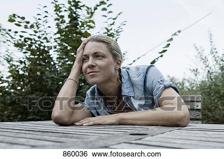 A woman sitting at an outdoor table, non-urban scene View Large Photo Image Stock Photograph - A woman sitting at an outdoor table, non-urban scene. Fotosearch