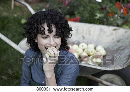 Stock Image - A woman taking a bite from a freshly picked apple. Fotosearch