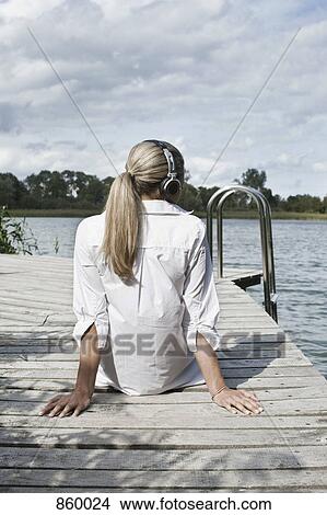 A woman wearing headphones relaxing on a jetty View Large Photo Image Picture - A woman wearing headphones relaxing on a jetty. Fotosearch