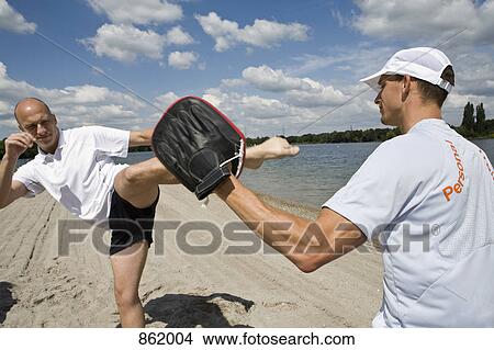 A man kick boxing with a personal trainer on the beach View Large Photo Image Picture - A man kick boxing with a personal trainer on the beach. Fotosearch