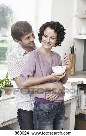 Picture - A couple embracing in the kitchen. Fotosearch