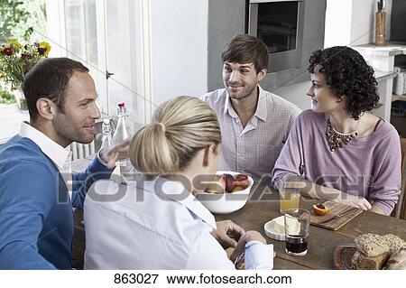 Stock Photo - A group of friends sitting at the dining table together. Fotosearch