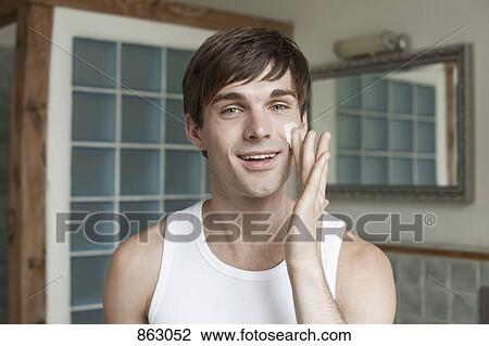 Stock Image - A man applying face cream in the bathroom. Fotosearch