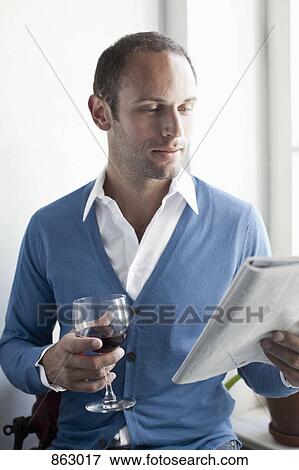 Stock Photo - A man drinking a glass of wine and reading a magazine. Fotosearch