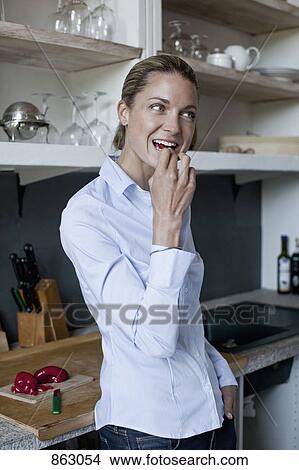 A woman eating a piece of red pepper in the kitchen View Large Photo Image Picture - A woman eating a piece of red pepper in the kitchen. Fotosearch