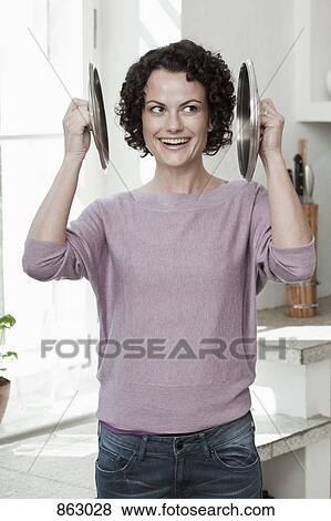Stock Photo - A woman holding two pan lids to her ears. Fotosearch