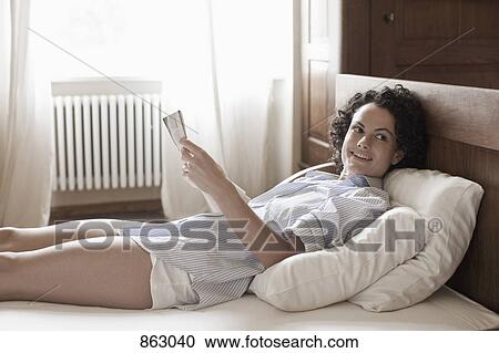 A woman lying down and reading on her bed View Large Photo Image Stock Image - A woman lying down and reading on her bed. Fotosearch