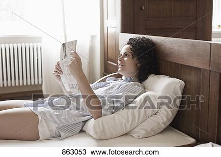 Stock Image - A woman lying on her bed and reading the newspaper. Fotosearch