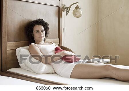 A woman lying on her bed with a hot water bottle on her stomach View Large Photo Image Stock Image - A woman lying on her bed with a hot water bottle on her stomach. Fotosearch