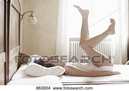A woman lying on her bed with her legs in the air View Large Photo Image Picture - A woman lying on her bed with her legs in the air. Fotosearch