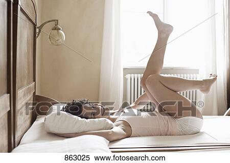 Stock Photography - A woman lying on her bed with her legs in the air. Fotosearch