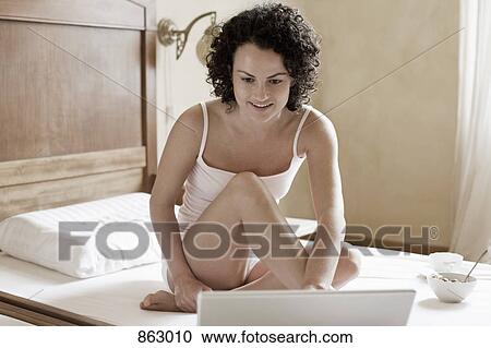 A woman sitting on her bed and using her laptop View Large Photo Image Stock Image - A woman sitting on her bed and using her laptop. Fotosearch