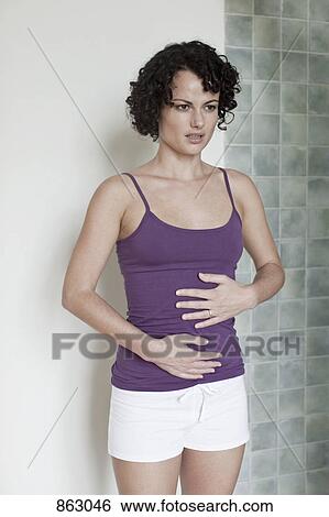 A woman standing touching her stomach View Large Photo Image Stock Photograph - A woman standing touching her stomach. Fotosearch