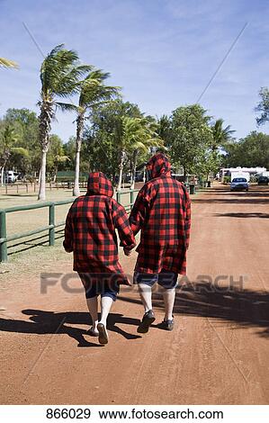 Stock Photo - Rear view of two people dressed in red checked jackets walking down a dirt road. Fotosearch