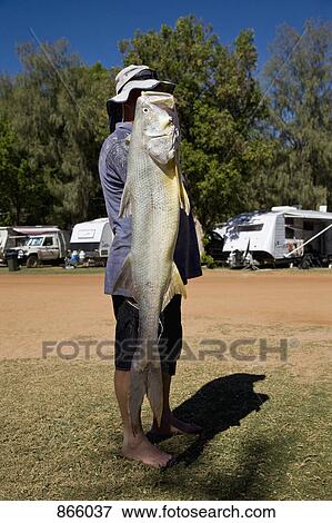 Stock Photo - Side view of a man holding a large fish. Fotosearch