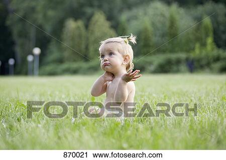 Stock Image - A baby girl sitting on grass in a diaper and looking confused. Fotosearch