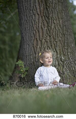 Stock Photograph - A baby girl sitting under a tree and looking away. Fotosearch