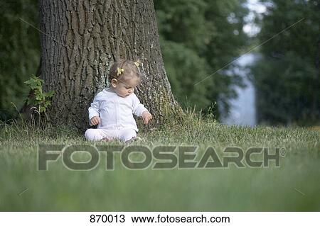 Stock Image - A baby girl sitting under a tree. Fotosearch
