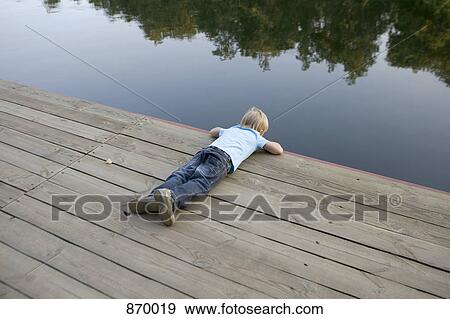 A boy looking into the water from a wooden jetty View Large Photo Image Stock Photo - A boy looking into the water from a wooden jetty. Fotosearch