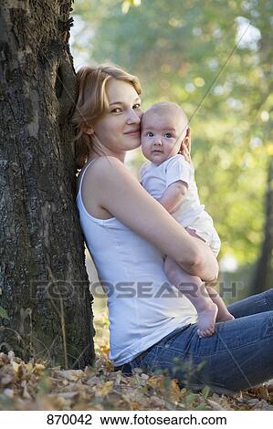 A mother sitting against a tree kissing her baby, looking at camera View Large Photo Image Stock Image - A mother sitting against a tree kissing her baby, looking at camera. Fotosearch