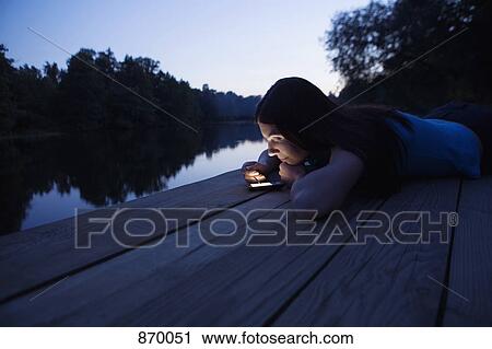 A woman using an electronic organizer while lying on a jetty, dusk View Large Photo Image Stock Image - A woman using an electronic organizer while lying on a jetty, dusk. Fotosearch