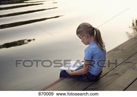 A young girl sitting at the edge of a jetty and reading a book View Large Photo Image Stock Photo - A young girl sitting at the edge of a jetty and reading a book. Fotosearch