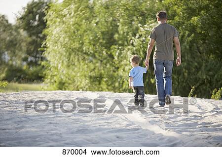 Rear view of a man and a young boy walking hand in hand View Large Photo Image Picture - Rear view of a man and a young boy walking hand in hand. Fotosearch
