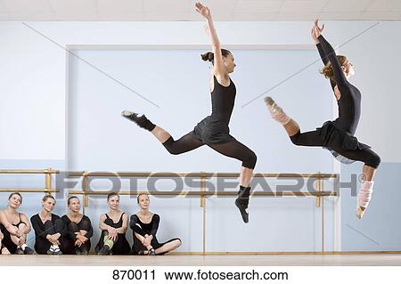 Stock Image - Two ballerinas leaping through the air as others look on. Fotosearch