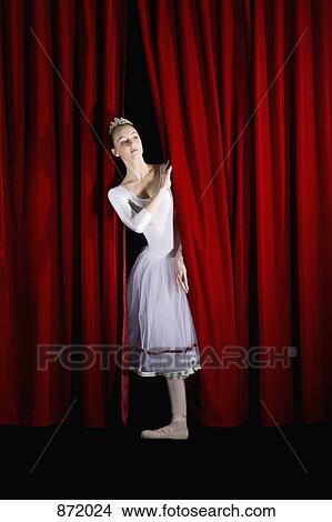 Picture - A ballet dancer peeking through a stage curtain, front view. Fotosearch