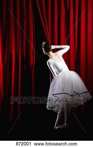 Stock Image - A ballet dancer peeking through a stage curtain, rear view. Fotosearch