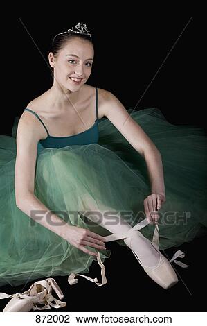 Stock Image - A ballet dancer wearing a costume tying her pointe shoe. Fotosearch