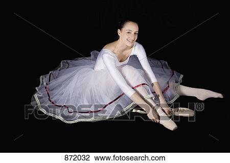 Stock Image - A smiling ballet dancer putting on her pointe shoe. Fotosearch