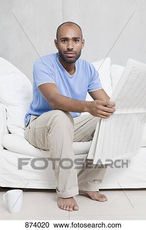 A man sitting on a sofa holding a newspaper View Large Photo Image Stock Image - A man sitting on a sofa holding a newspaper. Fotosearch