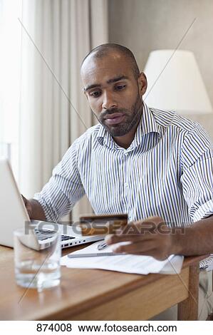 A man with a laptop looking at a credit card in his hand View Large Photo Image Stock Photo - A man with a laptop looking at a credit card in his hand. Fotosearch